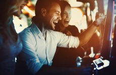 Closeup side view of a group of young adults playing slots in casino and having fun on weekend night.All standing by one machine and playing.Two couples on double date